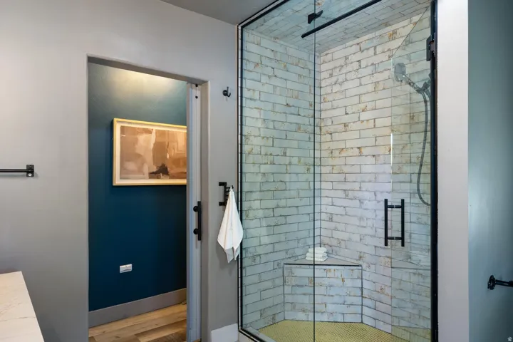 Glass-enclosed shower with subway tile walls and corner bench