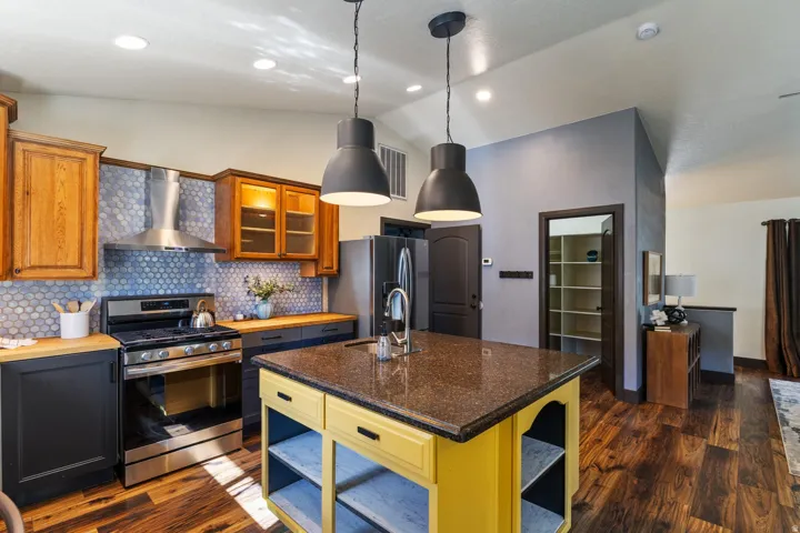 Kitchen featuring wood-finish flooring, stainless steel range with overhead vent, two-tone cabinetry, kitchen island with built-in shelving, and pendant lighting