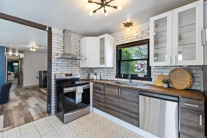 Contemporary kitchen featuring patterned floor tiles, a white brick-style backsplash, stainless steel appliances, wood-finish countertops, and white upper cabinetry with glass inserts
