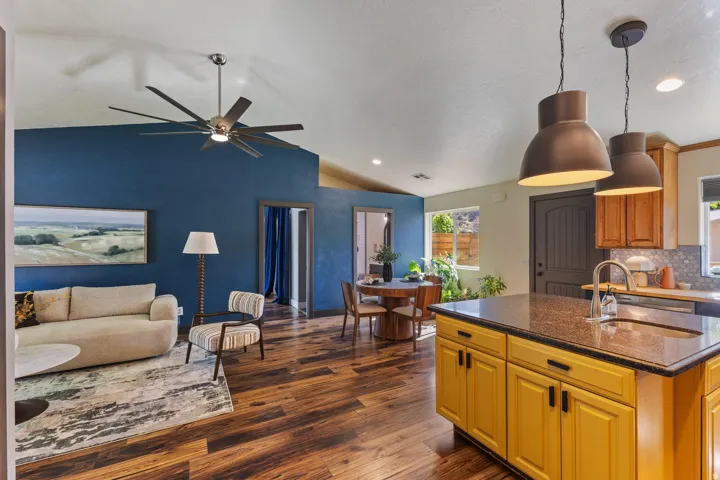Vaulted ceiling with a large ceiling fan, wood-finish flooring, a kitchen island with a built-in sink, pendant lighting, and a backsplash