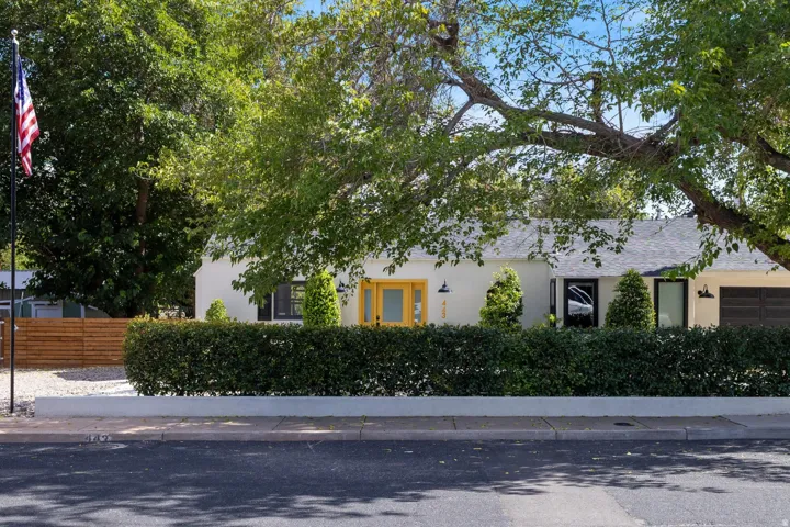 White stucco exterior with a gray shingled roof, featuring a vibrant yellow front door and black garage door