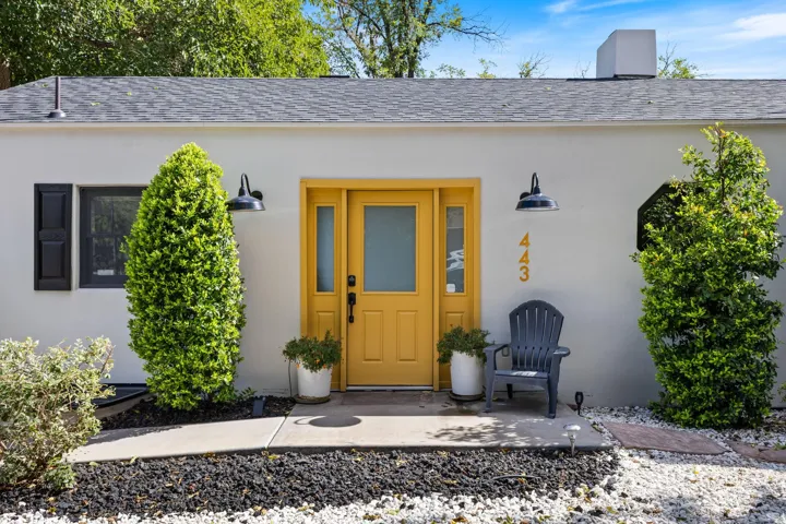 White stucco exterior with a vivid yellow front door, dual exterior wall sconces, and a gray shingle roof