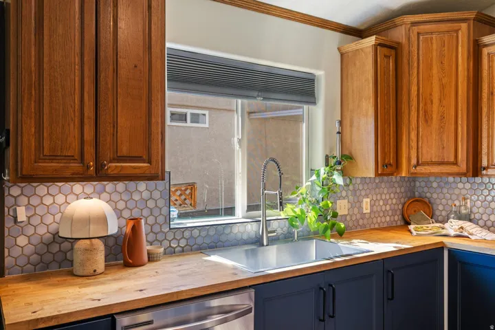 Stainless steel sink with a gooseneck faucet, light wood-finish countertops, two-tone cabinetry, and a hexagonal tile backsplash