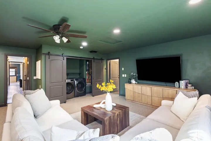 Integrated laundry area with sliding barn doors, a wood-finish media console, recessed lighting, and a ceiling fan