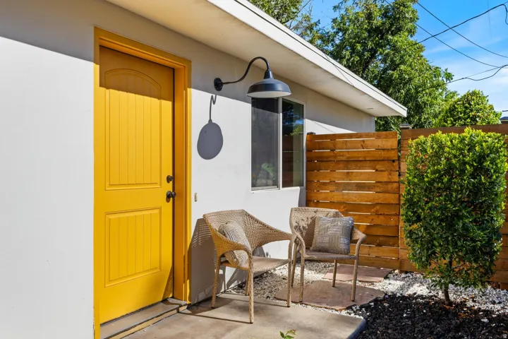 Exterior featuring a brightly painted entry door, wall-mounted light fixture, and a slatted wood privacy fence