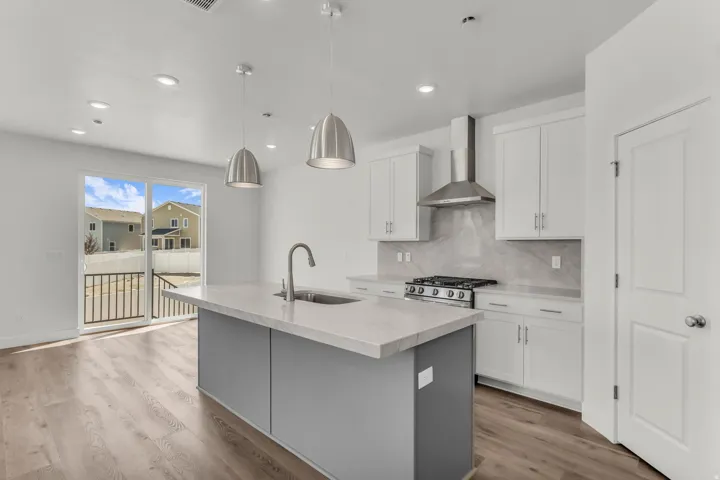 Modern kitchen featuring white cabinetry, a central island with a sink, stainless steel appliances, wood-finish flooring, and recessed lighting