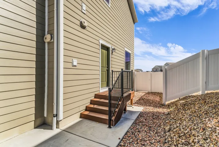 Siding exterior with a green entry door, concrete patio, and white privacy fencing