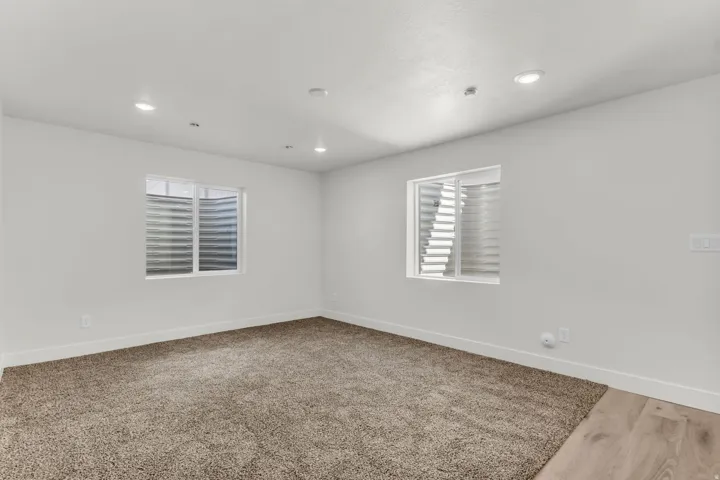 Recessed lighting, light-colored walls, two windows with blinds, plush carpeting, and wood-finish flooring
