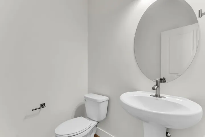 Pedestal sink with a single-handle faucet, round wall-mounted mirror, and a white toilet
