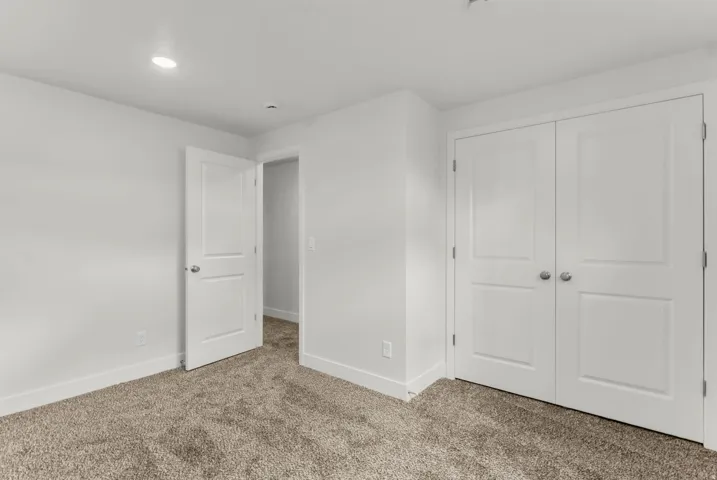 Plush carpet flooring, white painted walls, recessed ceiling lighting, and a double-door closet