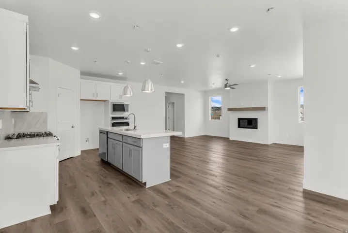 Open-concept living space with wood-finish flooring, recessed lighting, and a modern fireplace with a wooden mantel