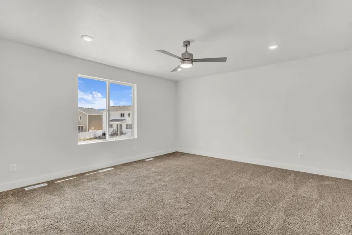 Spacious room featuring neutral carpeting, a large window, a ceiling fan with integrated lighting, and recessed ceiling lights