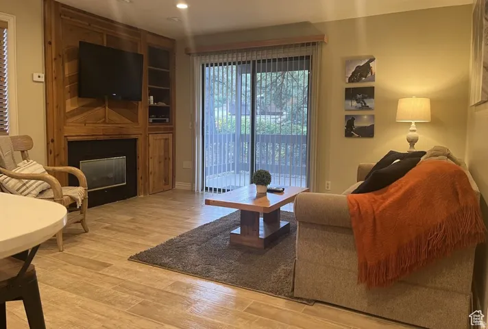 Built-in wood-finish media center with integrated fireplace, sliding glass door access to an outdoor patio, recessed lighting, and wood-finish flooring