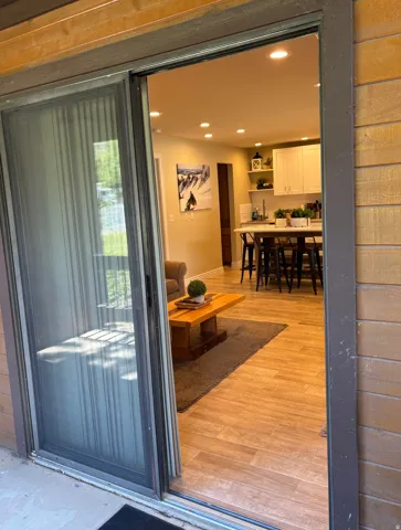 Sliding glass door entry to an open-concept living space with wood-finish flooring and recessed lighting
