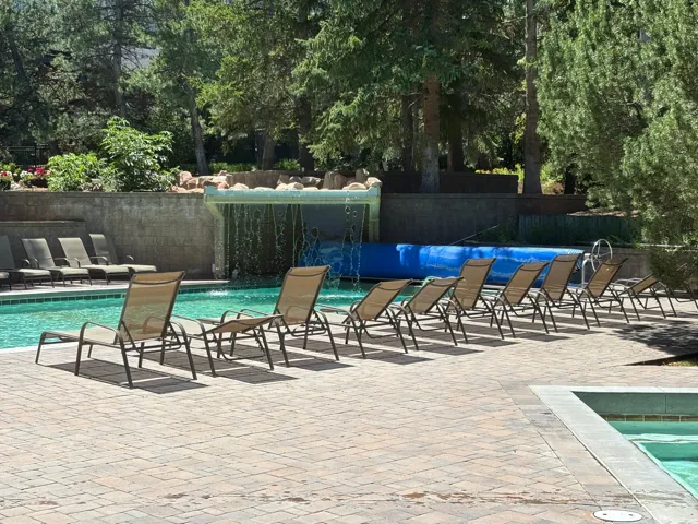 Swimming pool with a built-in rock waterfall feature, paver deck, and surrounding mature trees