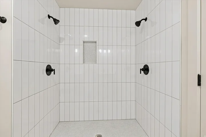 Shower stall featuring vertical subway tile, dual shower heads, dual matte black fixtures, and a recessed tile niche