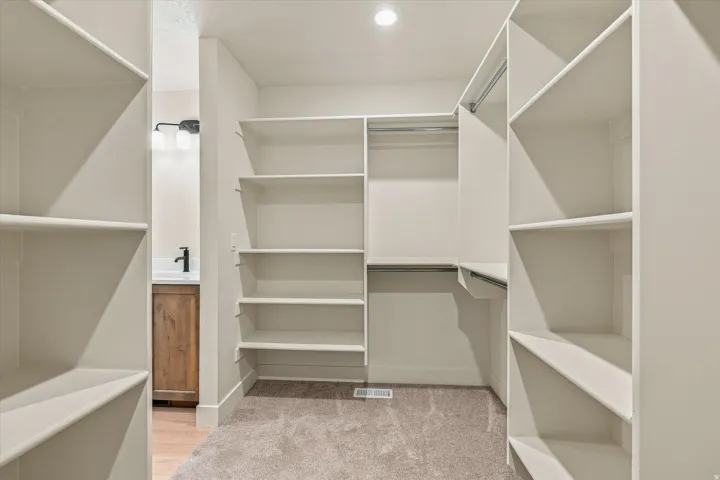 Recessed lighting, built-in shelving, hanging rods, carpet flooring, and a vanity with a wood-finish cabinet