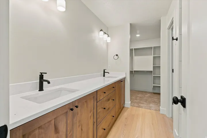 Dual vanity with wood-finish cabinetry, integrated sinks, white countertops, and matte black fixtures