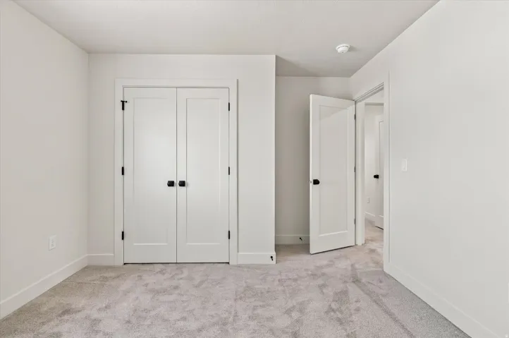 Light gray wall-to-wall carpeting, white walls, white trim, and white interior doors with black hardware