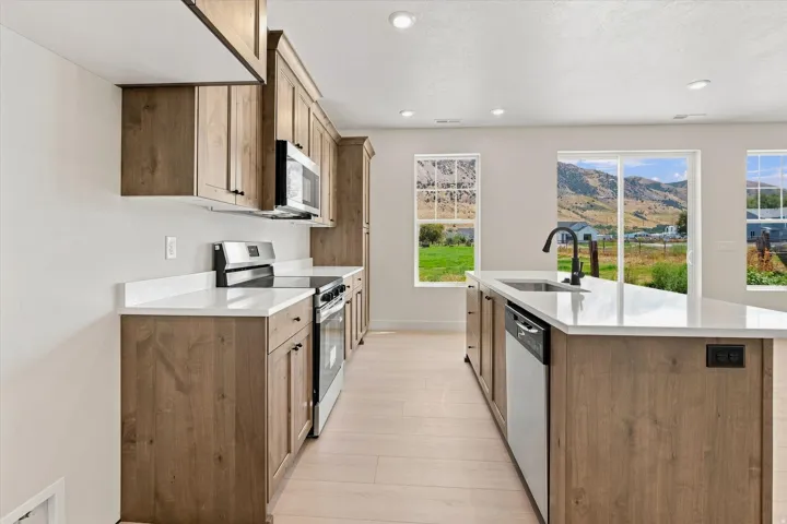 Kitchen featuring wood-finish cabinetry, stainless steel appliances, white countertops, and light wood-finish flooring