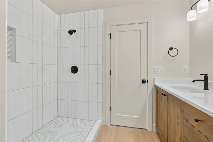 Walk-in shower with vertical subway tile, white penny tile floor, wood-finish vanity with built-in sink, white countertop, and matte black fixtures