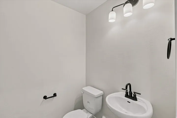 Pedestal sink with a matte black faucet, wall-mounted light fixture, and white wall finishes