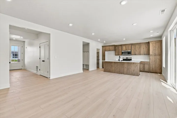 Light wood-finish flooring throughout, recessed lighting, and a kitchen featuring wood-grain cabinetry, an island with countertop, and stainless steel appliances