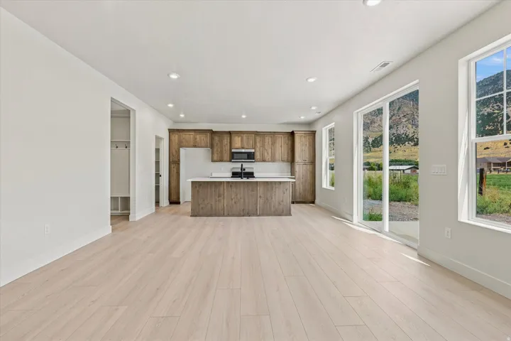 Spacious open-concept living area featuring light wood-finish flooring, a kitchen with wood cabinetry and a central island, and a sliding glass door to the exterior