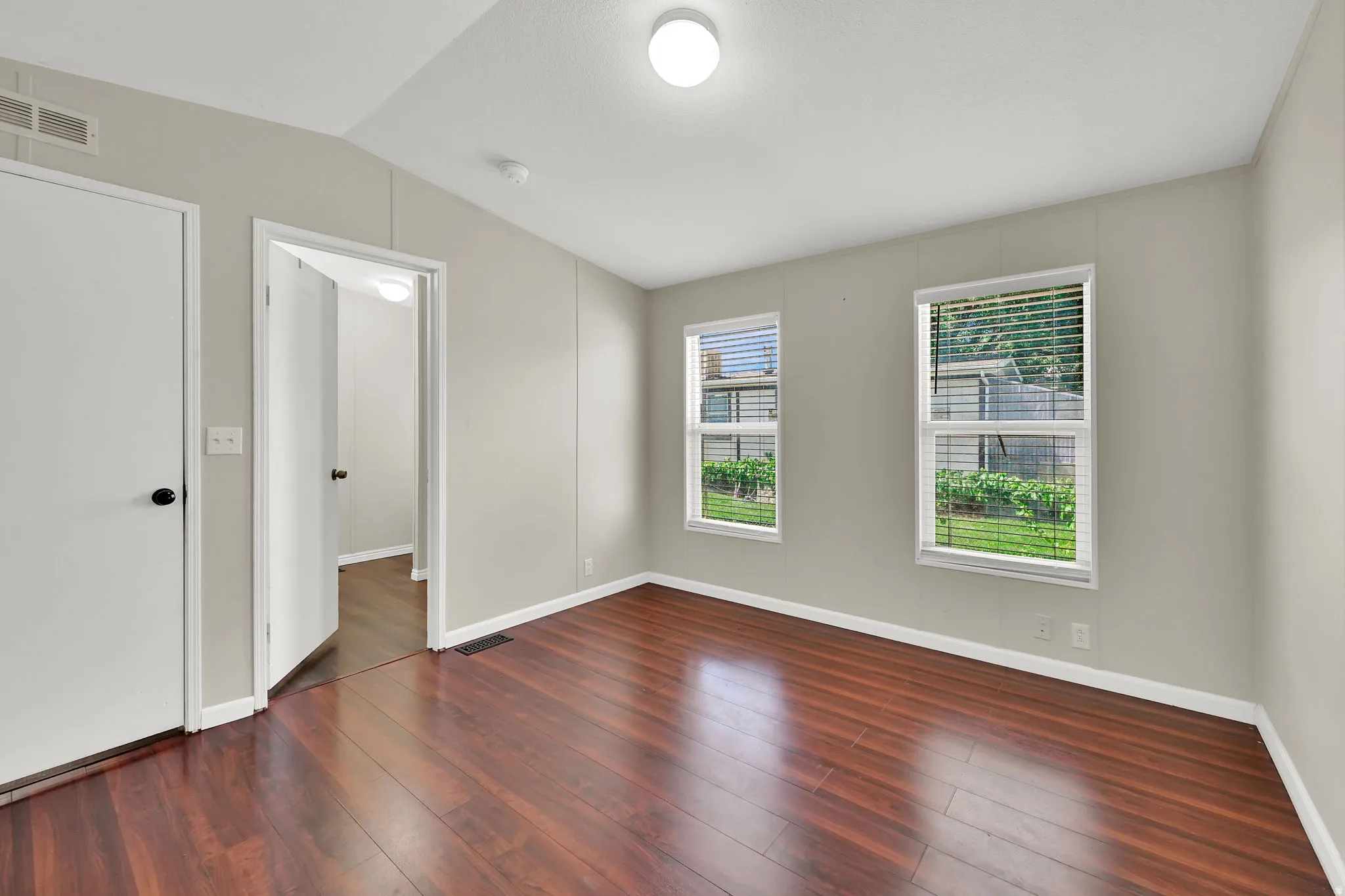 Wood-finish flooring, two windows with blinds, white trim, and a ceiling-mounted light fixture