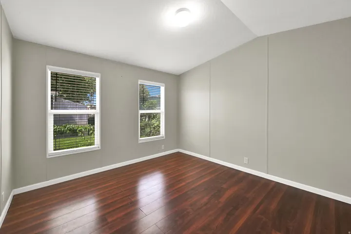 Wood-finish flooring, neutral wall paint, two single-hung windows with blinds, and an overhead flush-mount light fixture