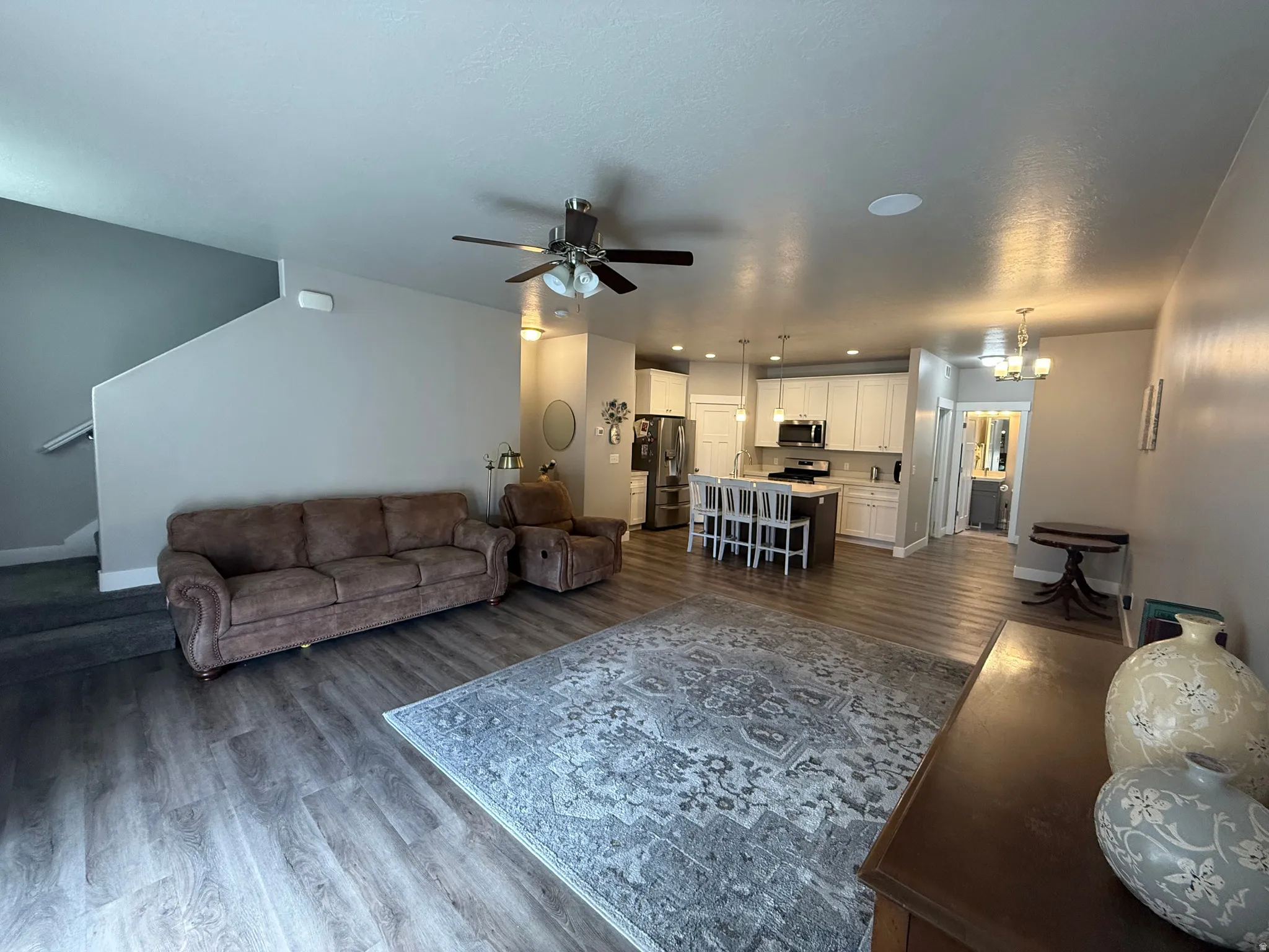 Open concept living area featuring wood-finish flooring, a ceiling fan, recessed lighting, and a kitchen with white cabinetry and a center island