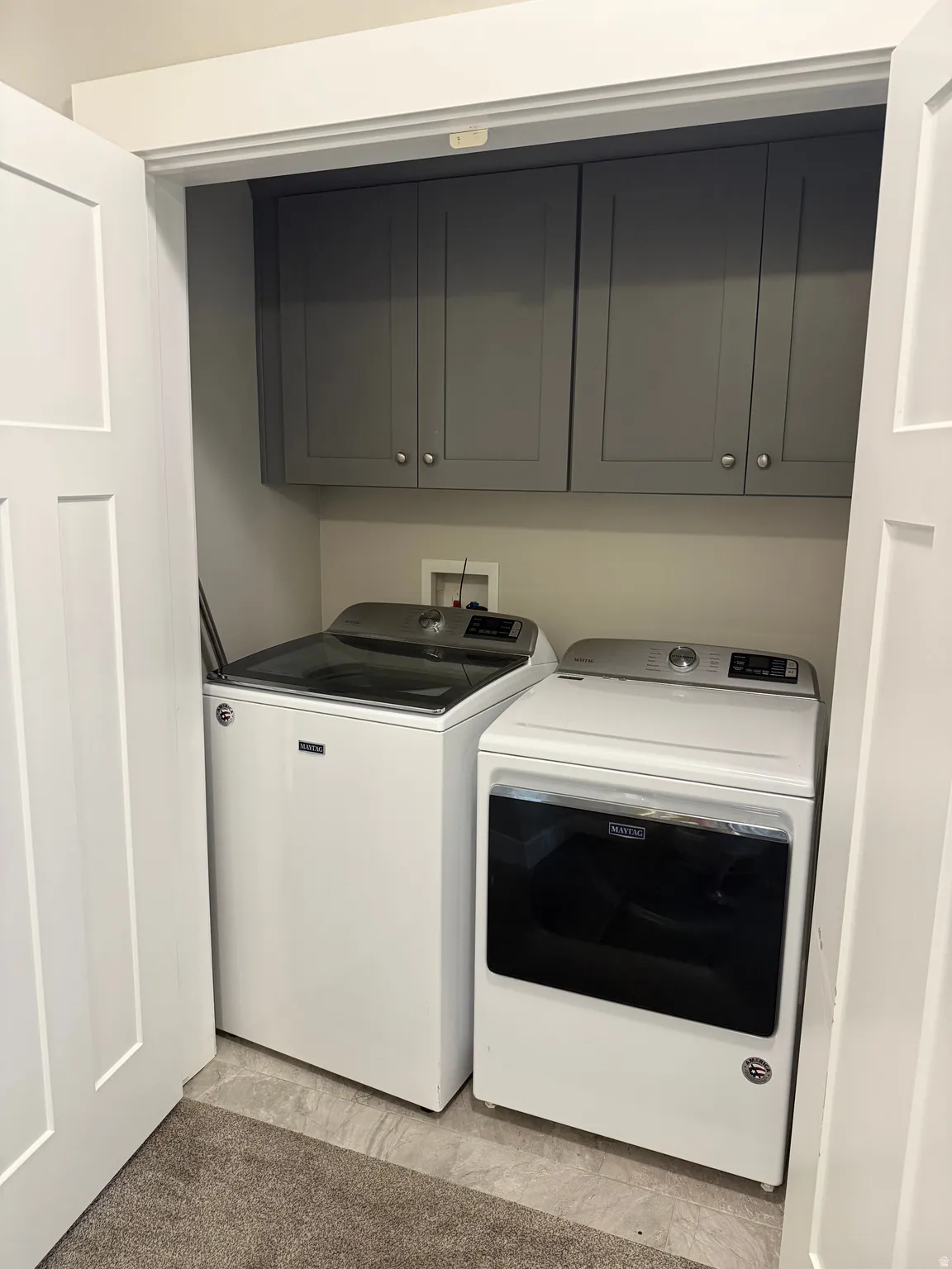 Enclosed laundry area featuring overhead cabinetry, a durable flooring surface, and paneled doors