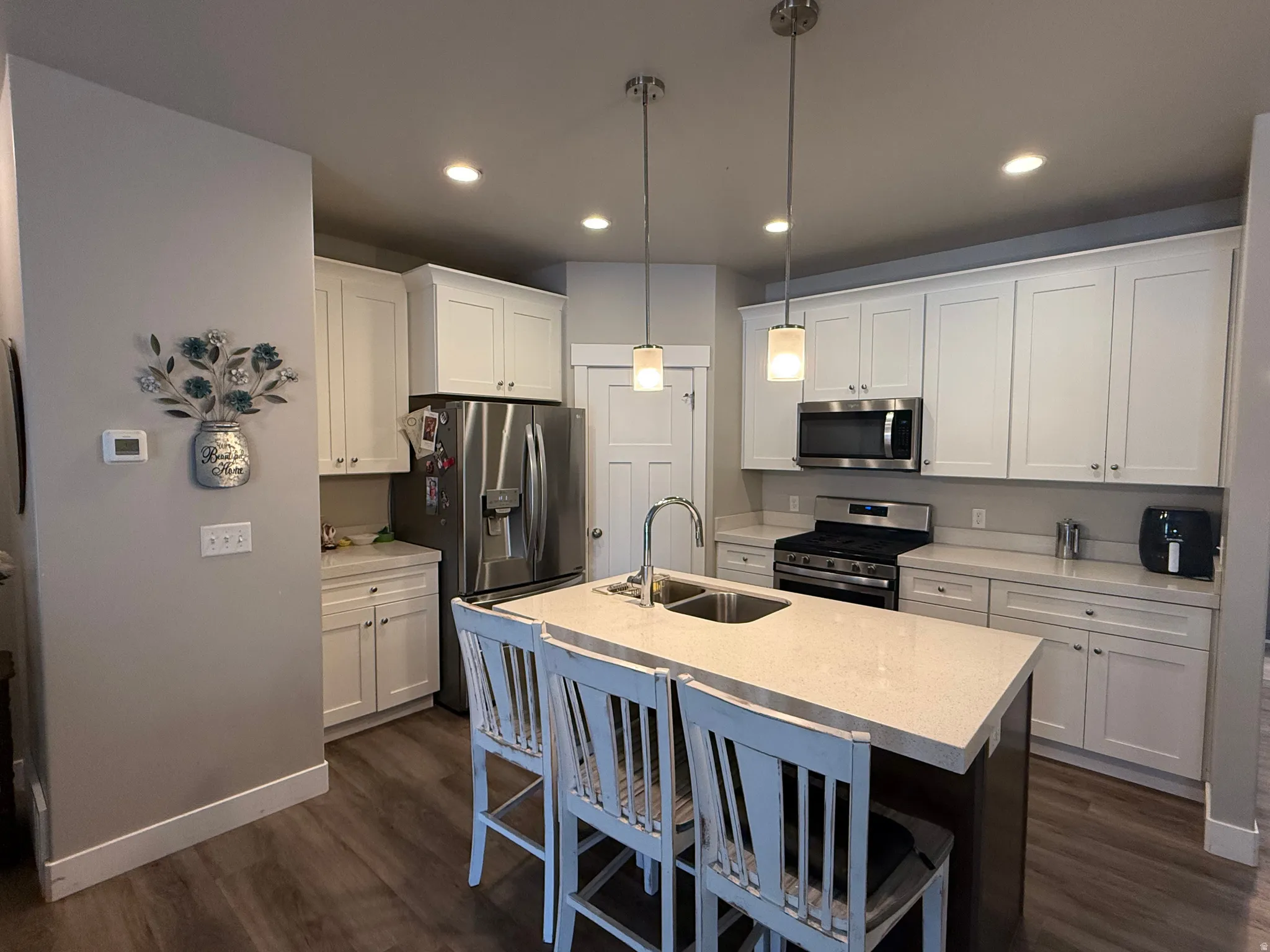 Modern kitchen featuring white shaker cabinetry, stainless steel appliances, a center island with sink, pendant lighting, and wood-finish flooring