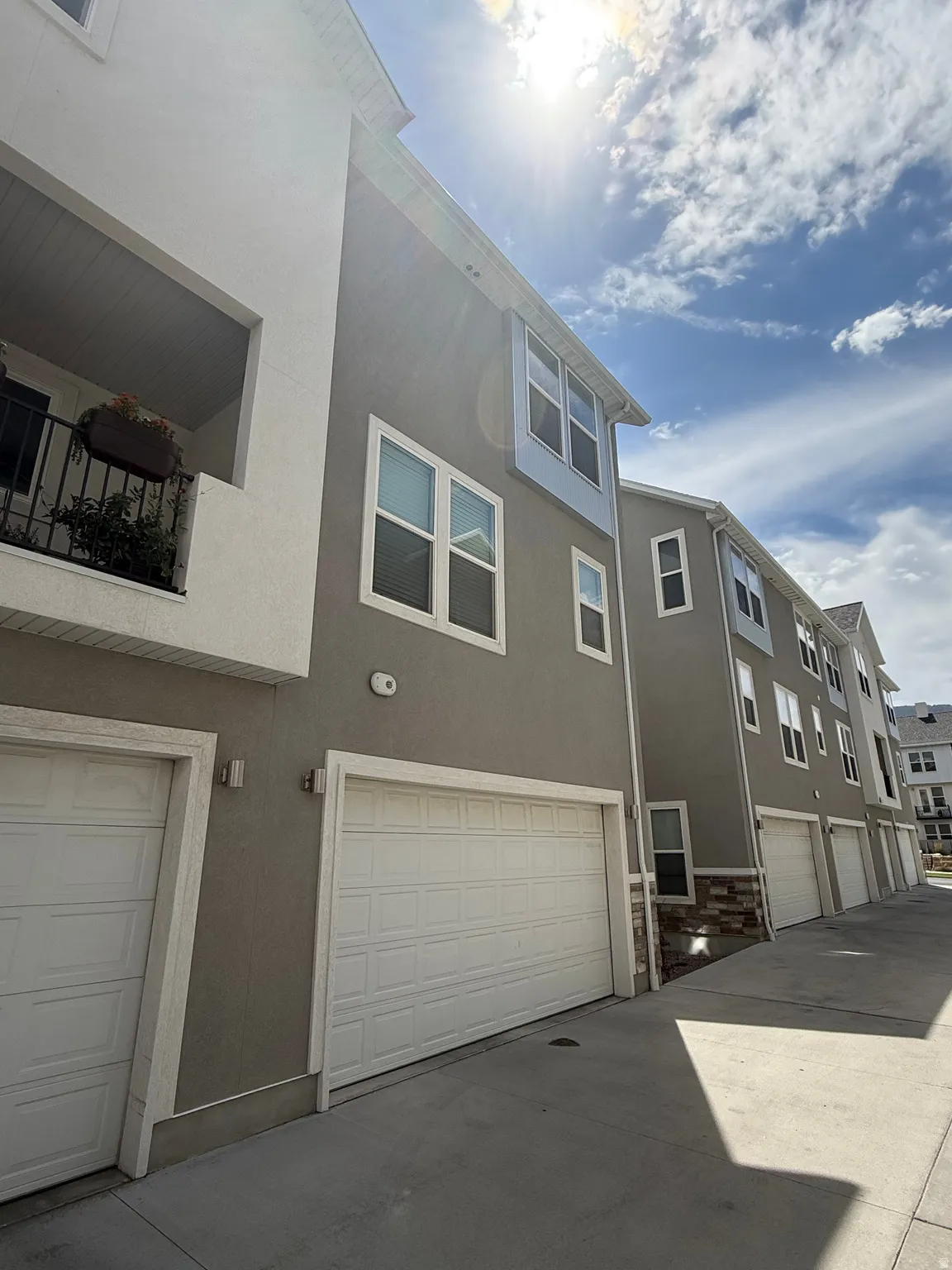 Neutral-toned stucco exterior with white trim, multi-pane windows, and a private balcony with iron railings