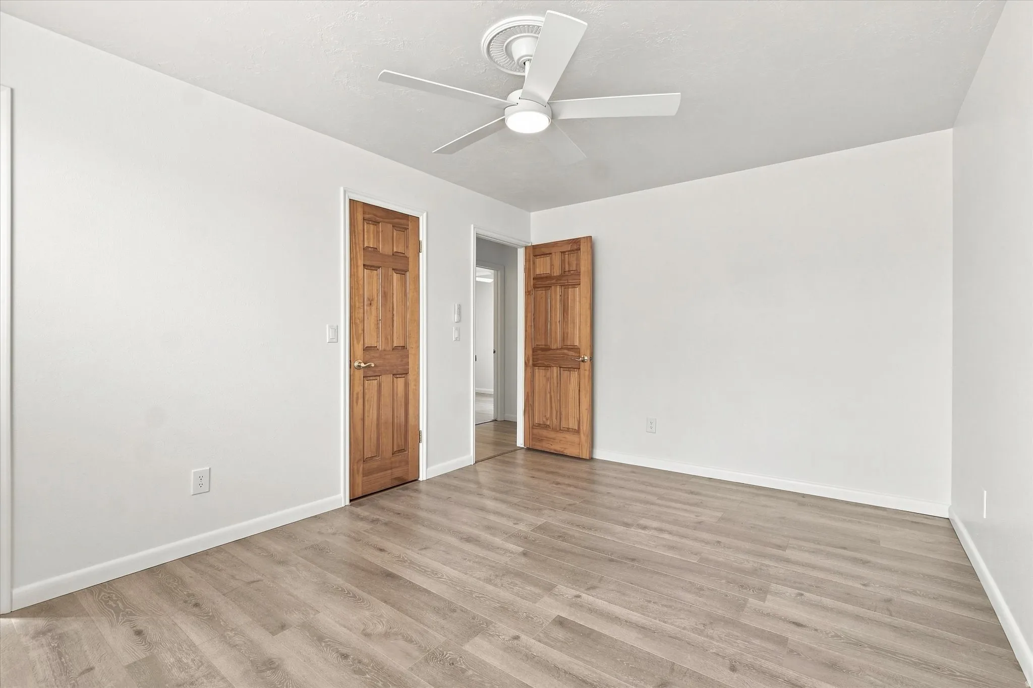Wood-finish flooring, white walls, and a ceiling fan with integrated lighting