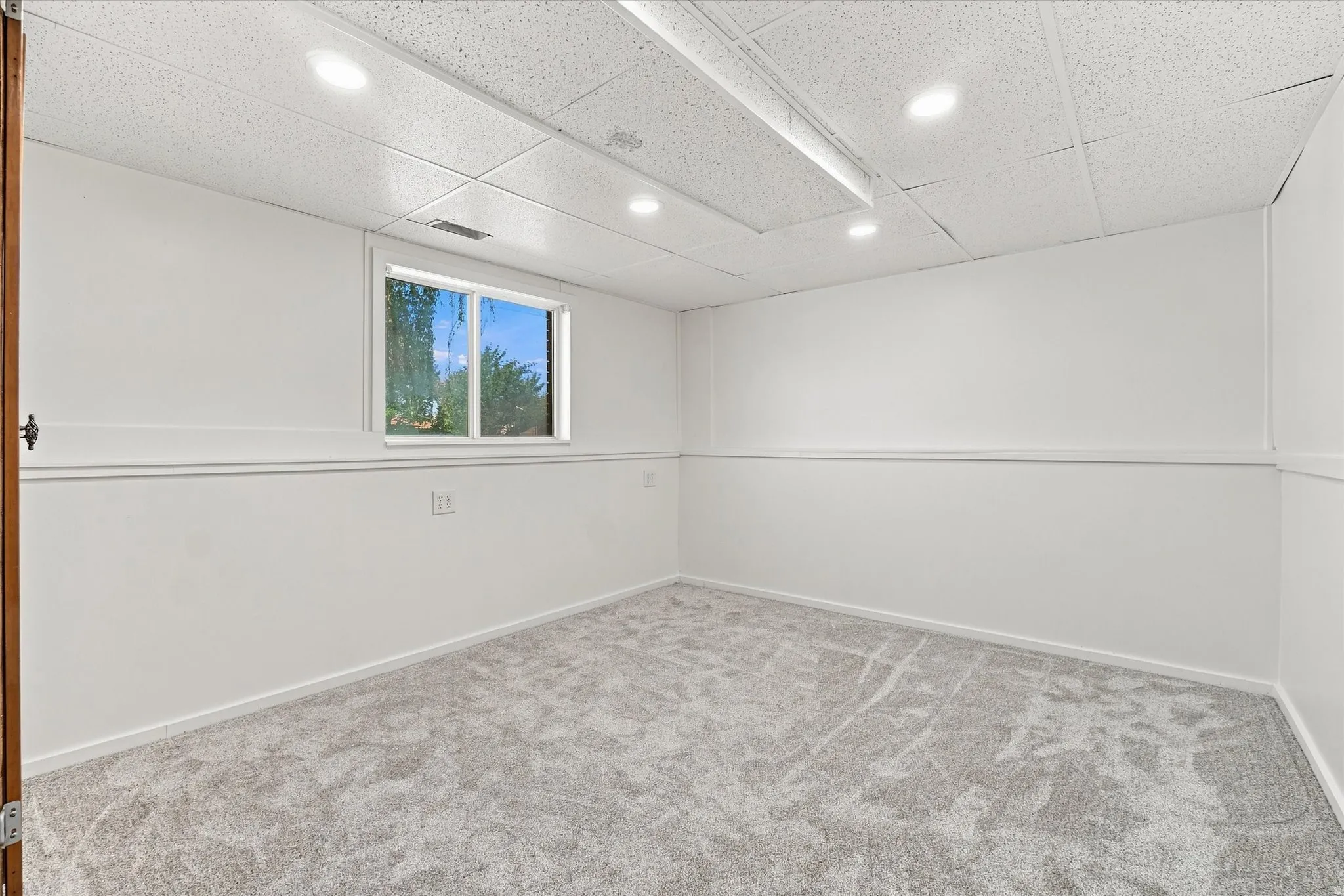 Recessed lighting, drop ceiling, wall paneling, window, and grey patterned carpeting