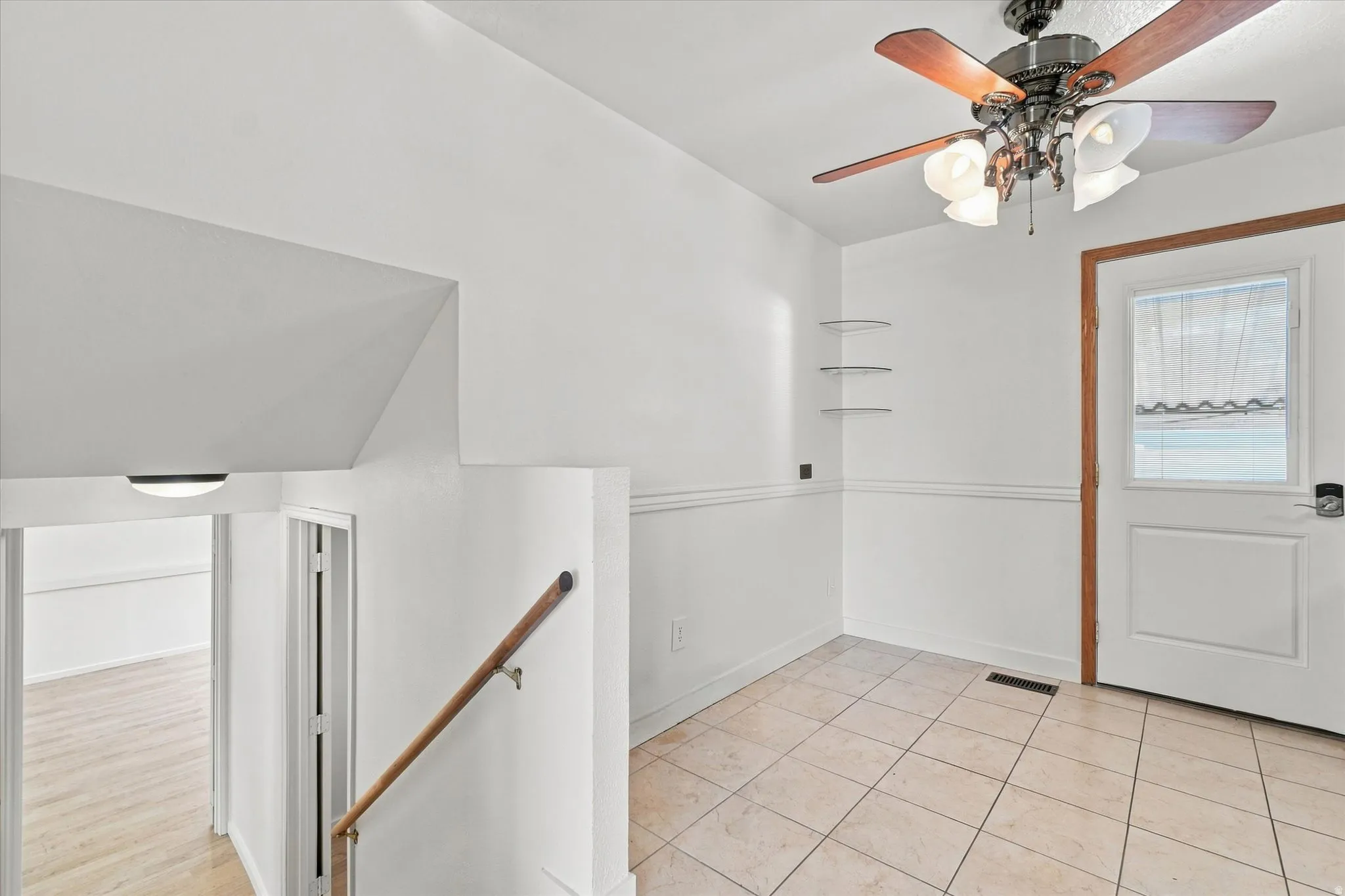 Tiled flooring, wood-finish ceiling fan with integrated lighting, wood-finish railing, and white wall paneling