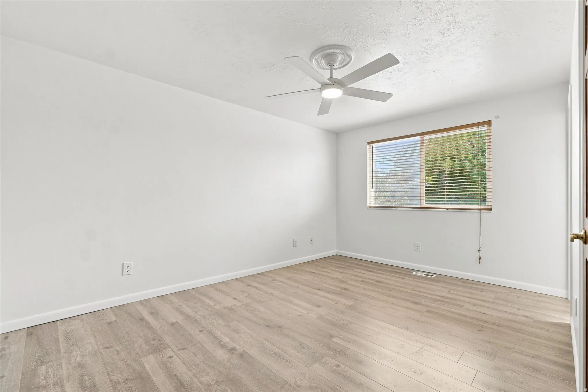Wood-finish flooring, white walls, ceiling fan, and a window with blinds