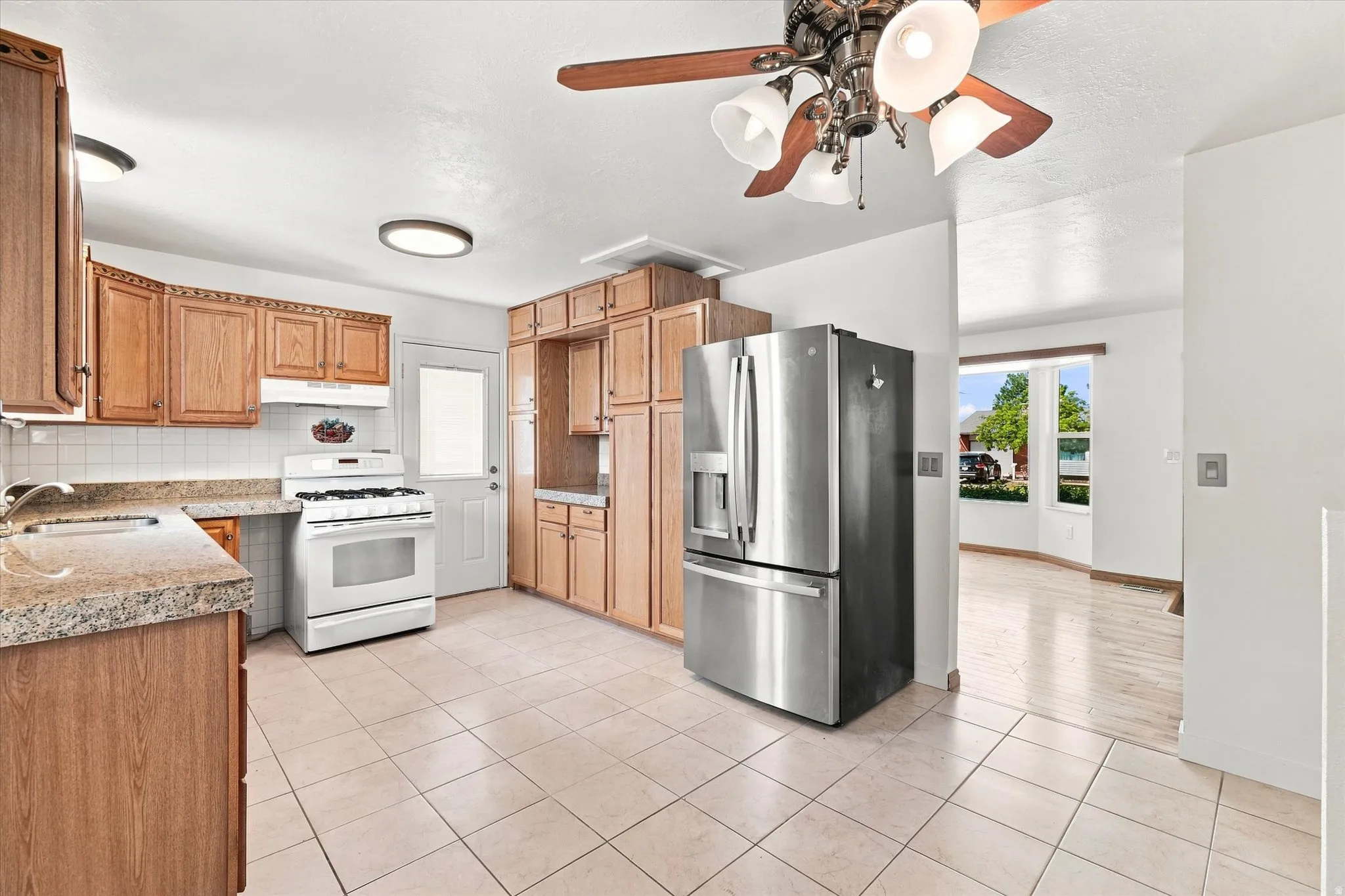 Tile flooring, wood-finish cabinetry, stainless steel refrigerator, white gas range, and a ceiling fan with integrated lighting