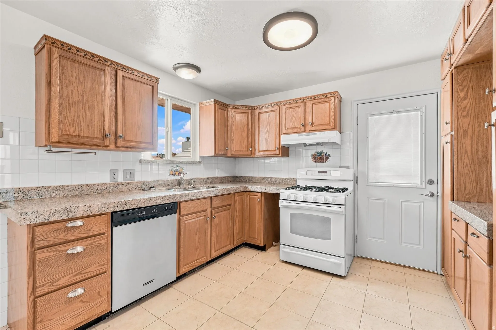 Kitchen featuring wood cabinetry, solid surface countertops, white tile backsplash, tile flooring, and a white gas range with coordinating hood