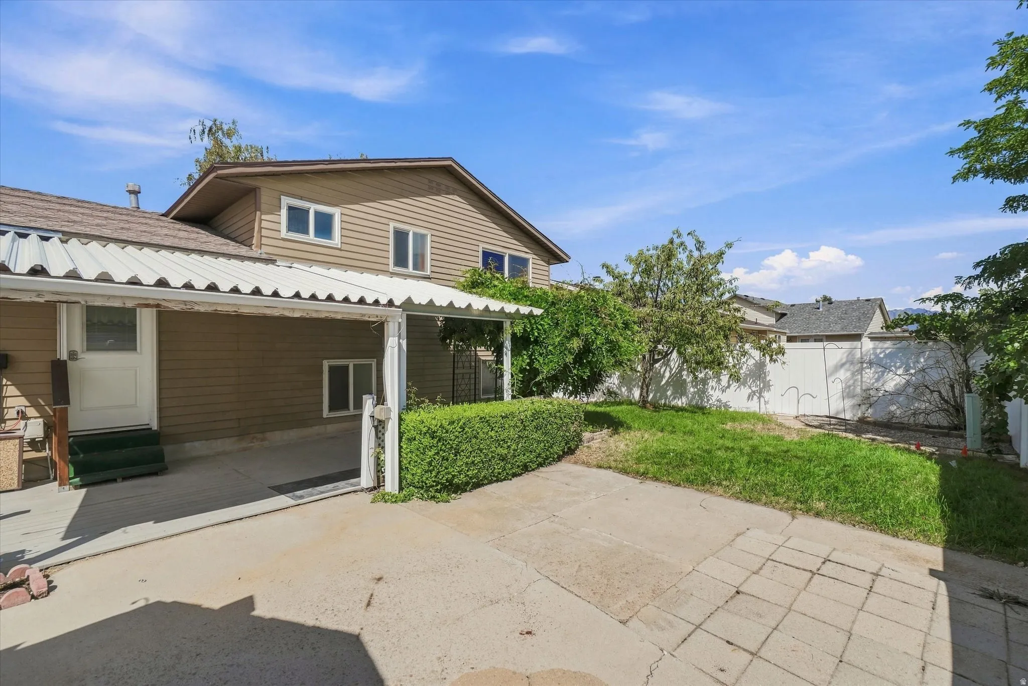 Carport with corrugated metal roof and concrete pad, vinyl siding exterior, and established landscaping