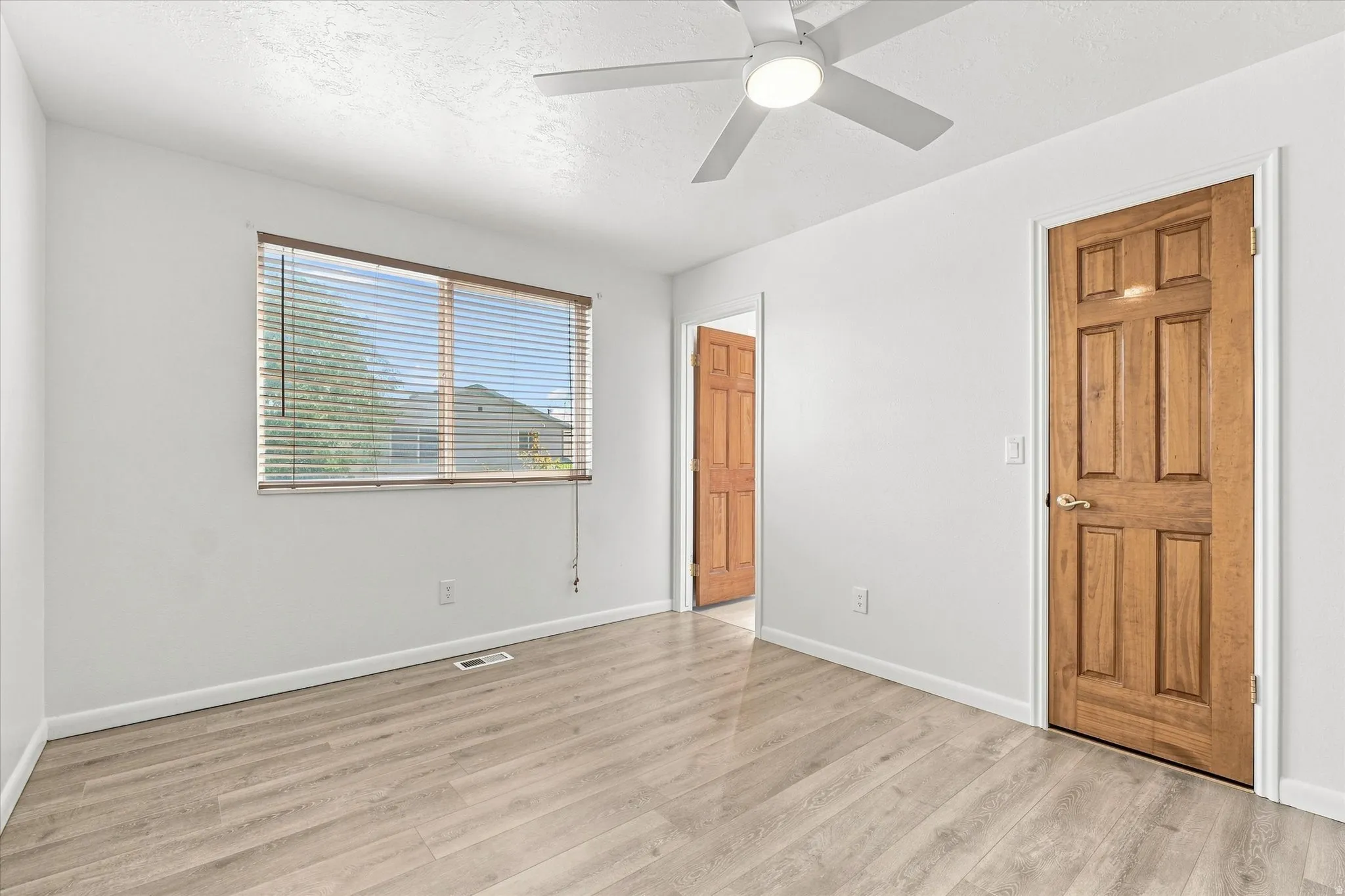 Light-filled room featuring wood-finish flooring, a window with blinds, and a ceiling fan with integrated lighting