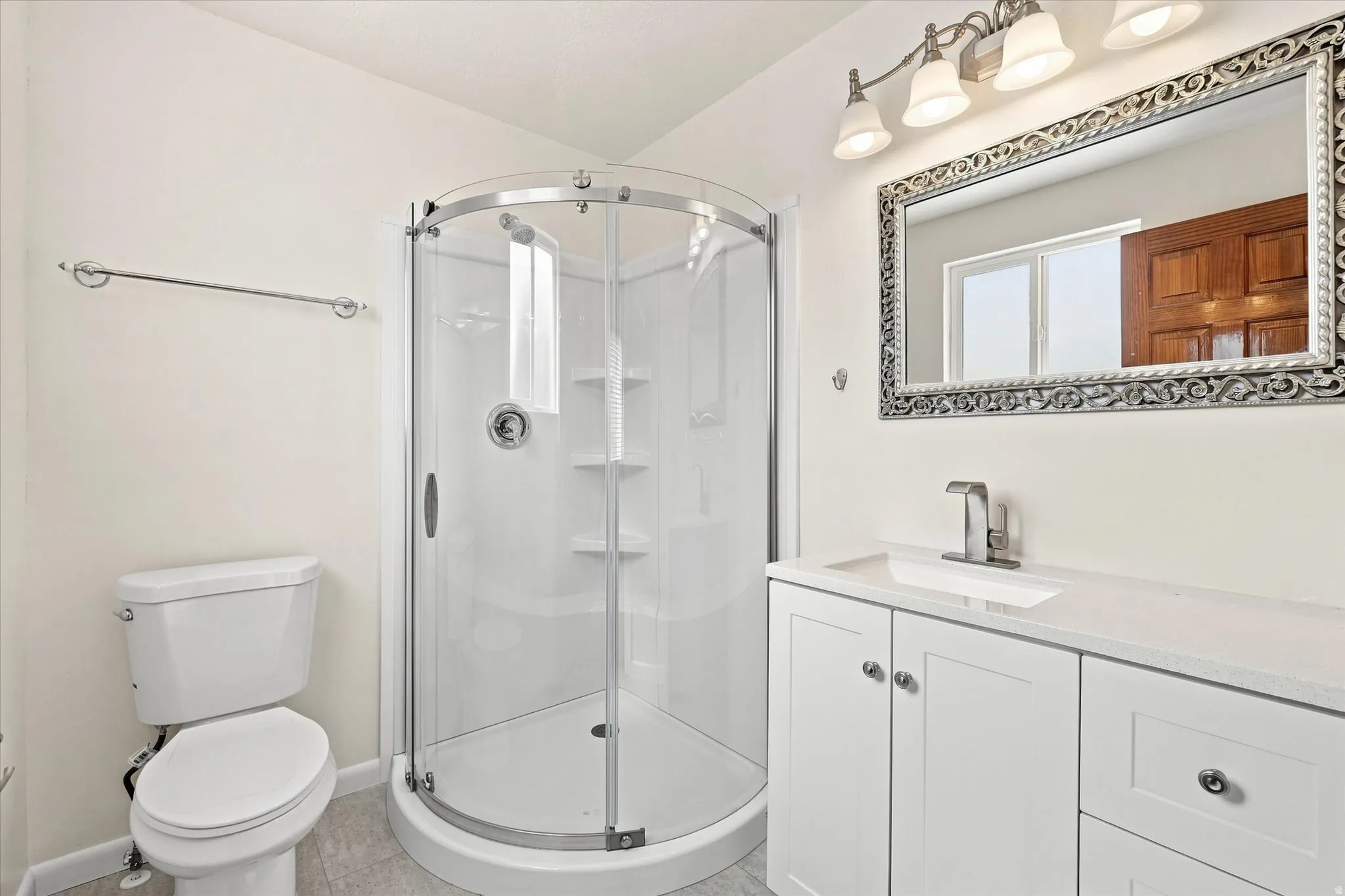 White vanity with undermount sink, a framed mirror, and a curved glass shower enclosure