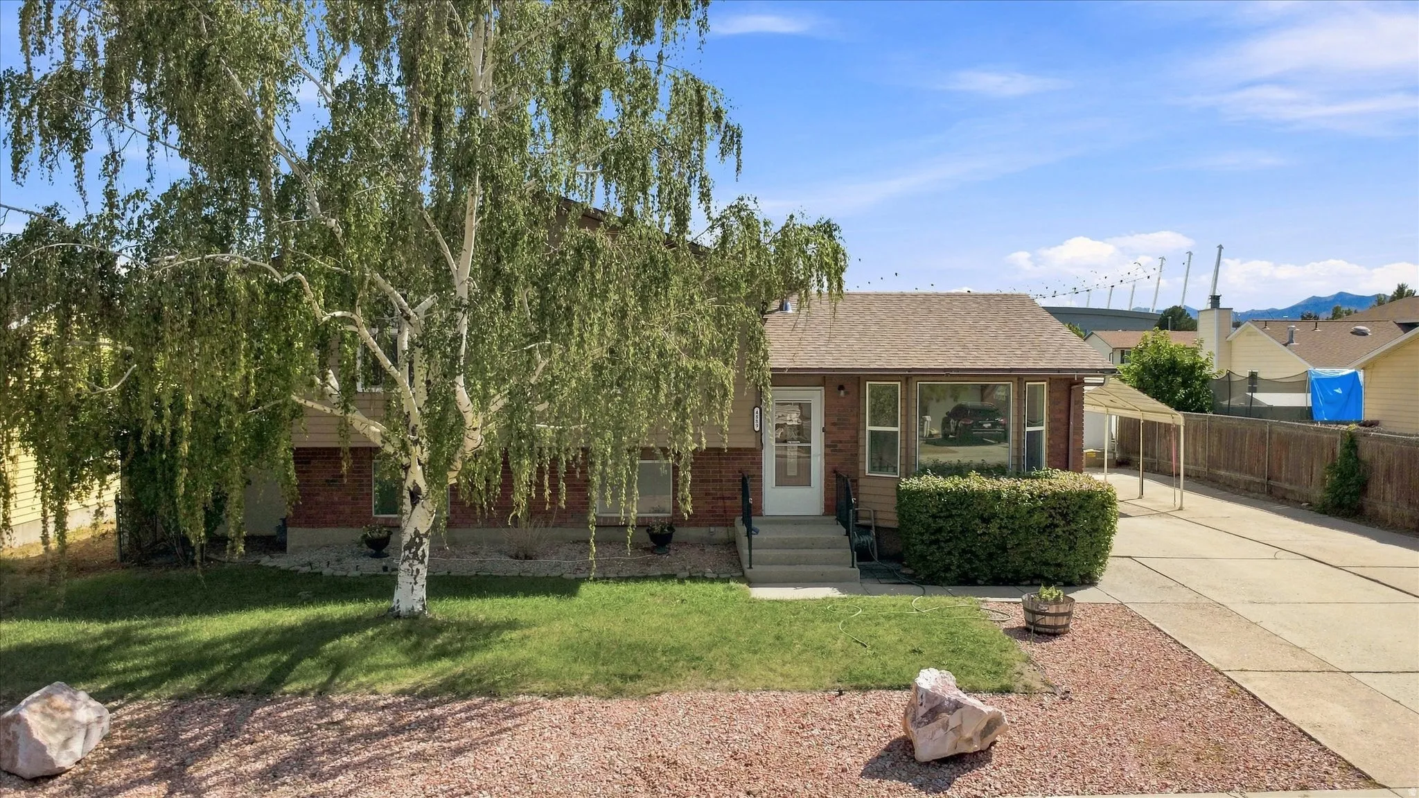 Brick and siding exterior with a pitched roof, front lawn, mature tree, and a concrete driveway leading to a carport