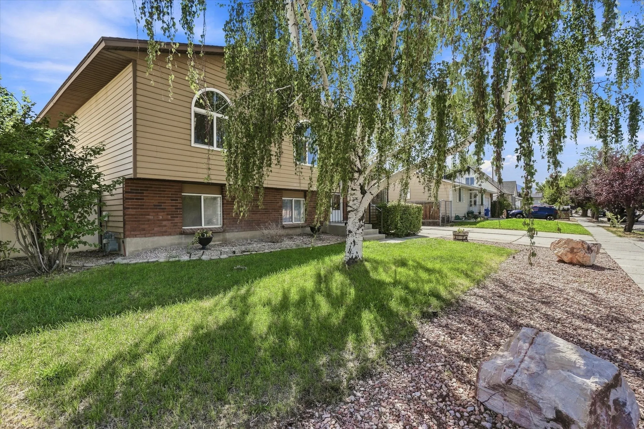 Split-level residence featuring brick and siding exterior, arched window, and a mature birch tree