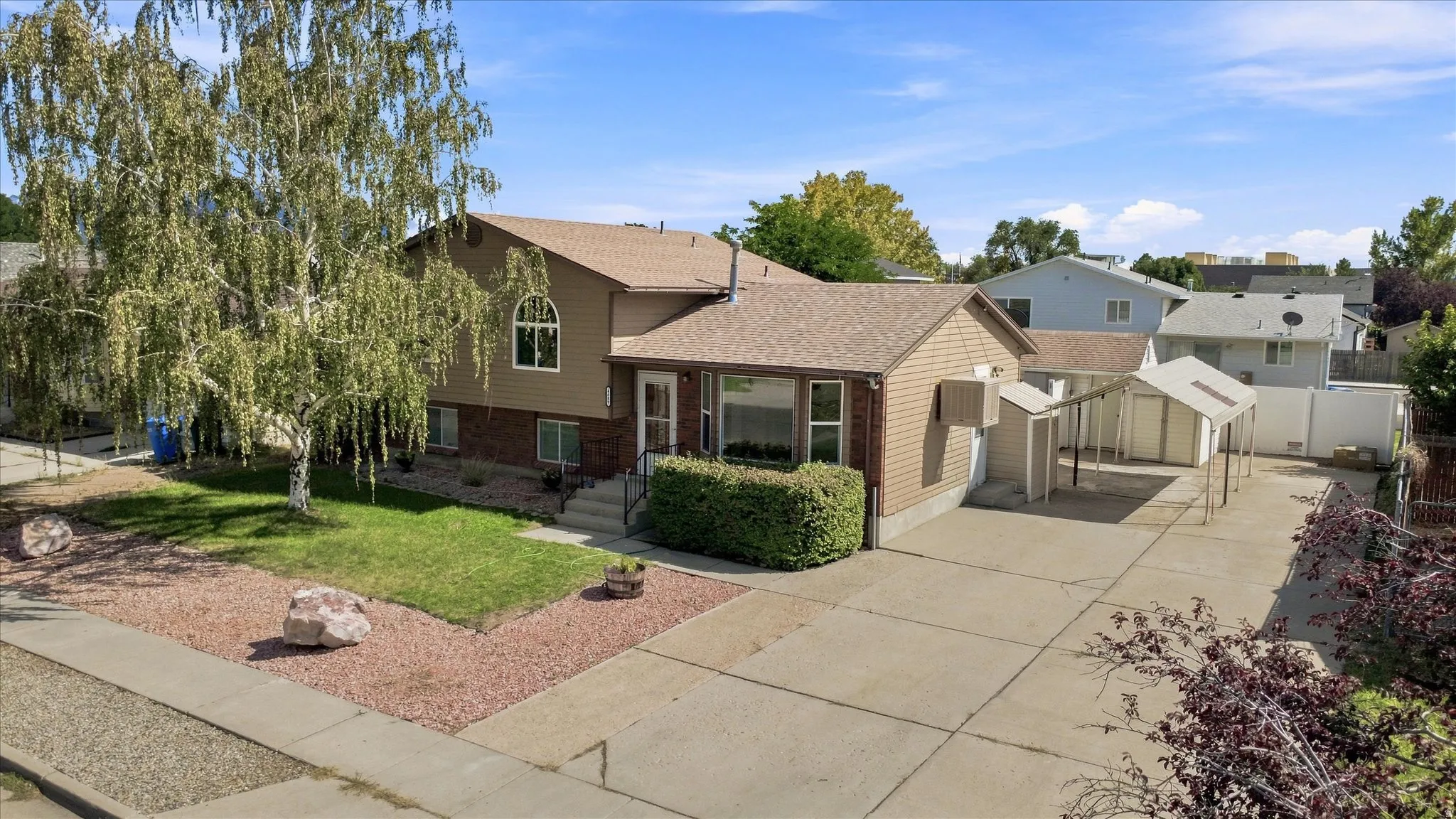 Split-level residence featuring a covered front entry, arched window, and a shed with an attached carport
