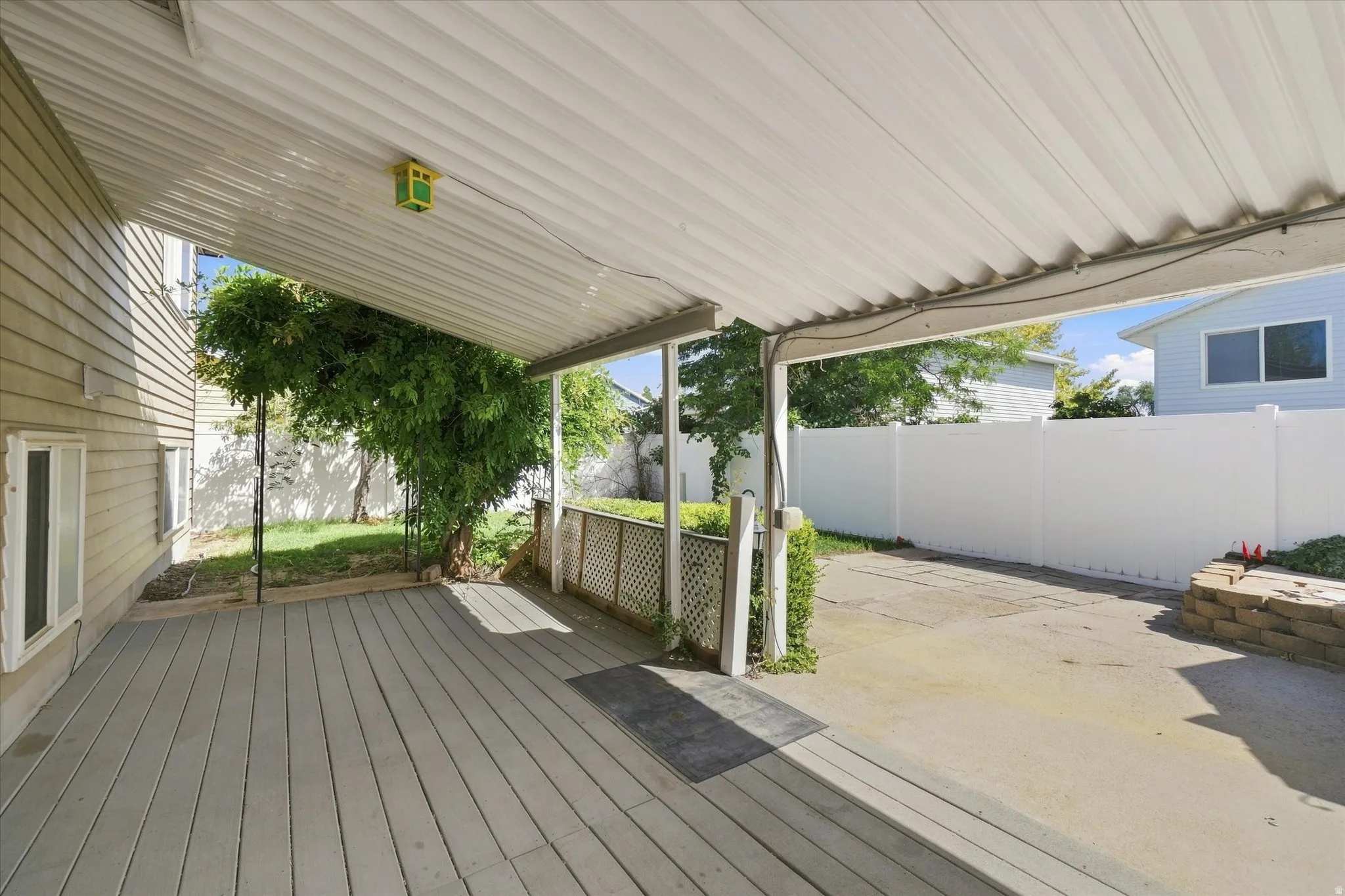 Covered patio with a composite deck, extending to a concrete pad, bordered by a white privacy fence