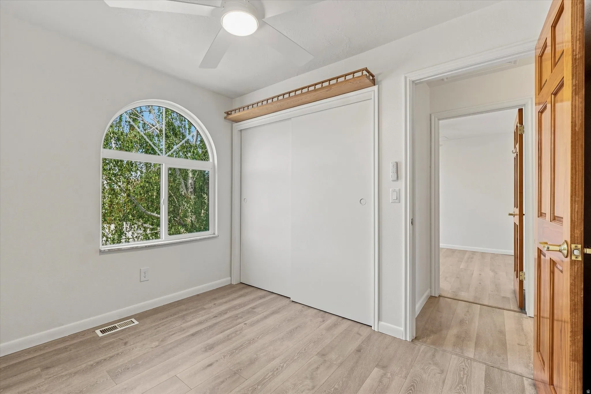 Arched window, wood-finish flooring, white ceiling fan, sliding closet doors, and a wood-paneled door