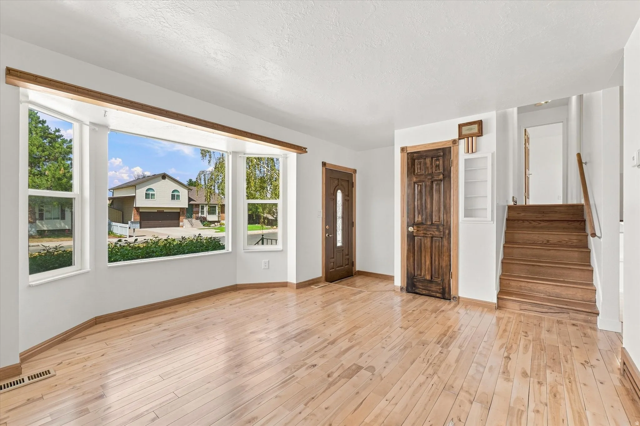 Hardwood flooring, bay window, natural wood trim, stained wood doors, and a wood staircase
