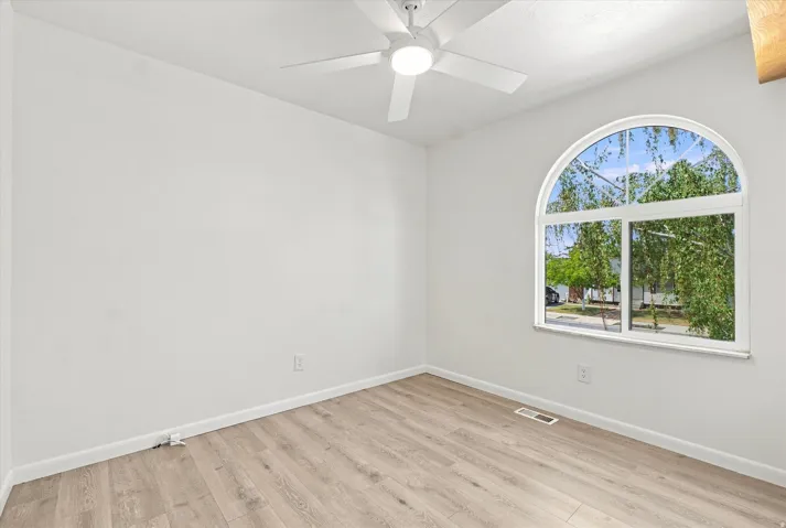 Arch-top window, wood-finish flooring, white walls, and a ceiling fan